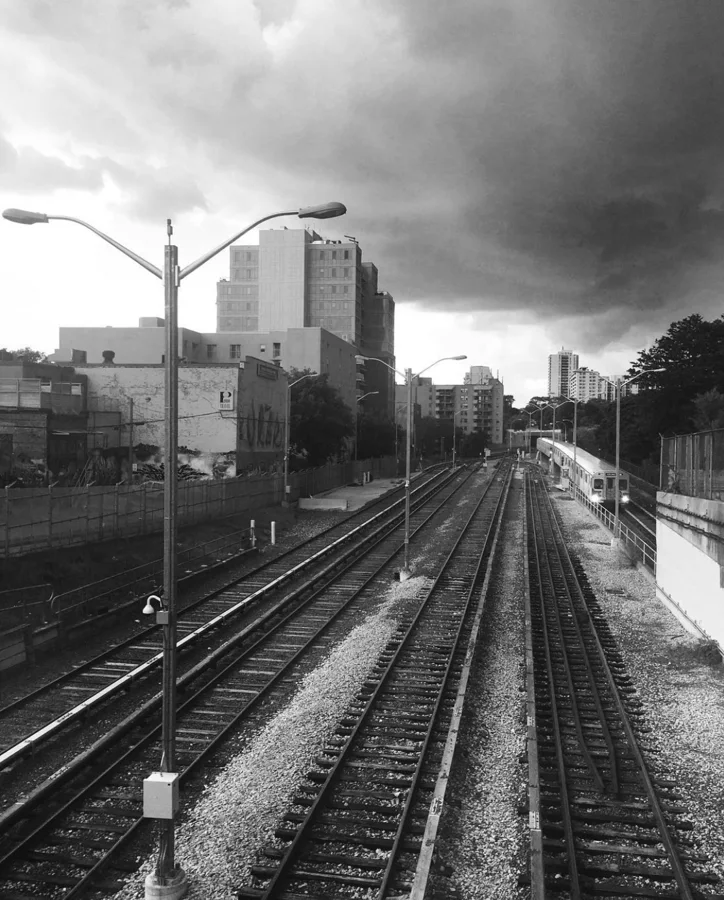 Black and white railway tracks beneath dark storm clouds
