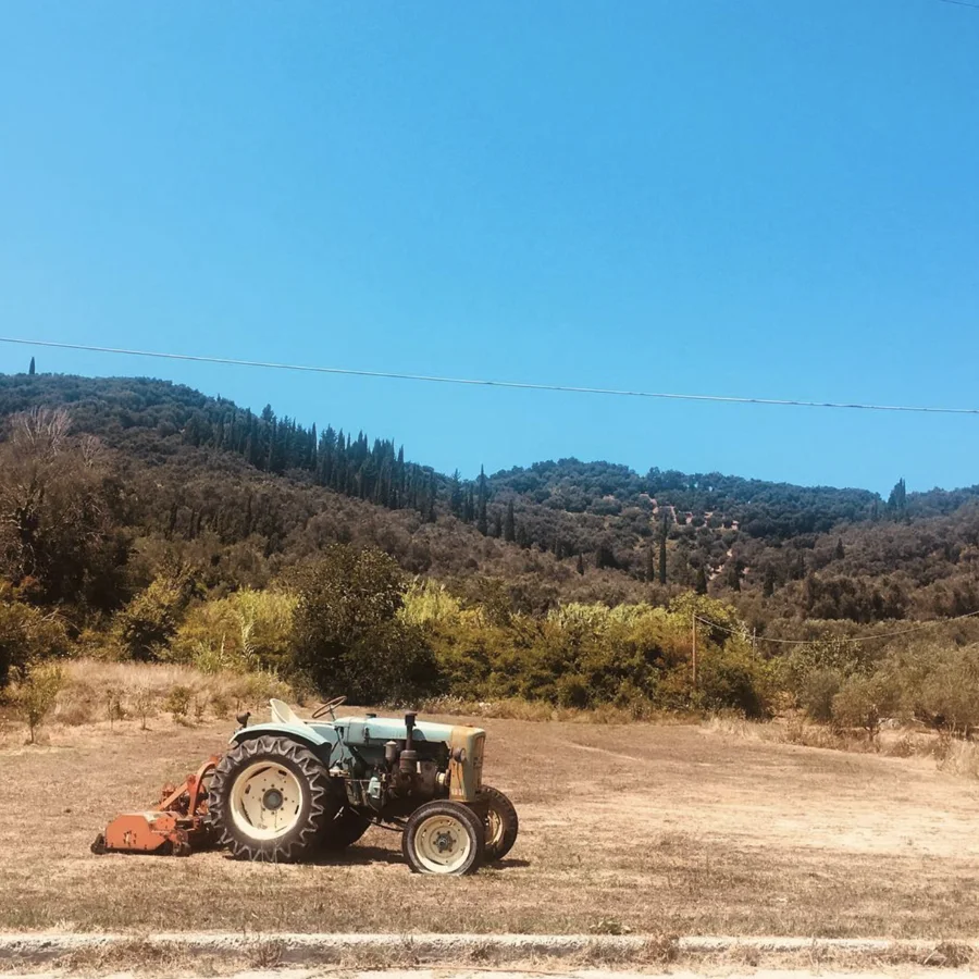 A vintage tractor in a dry field beneath wooded hills